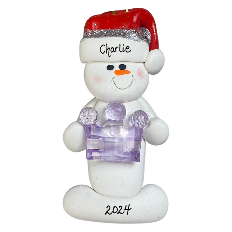 Ornament of white snowman in red hat holding purple plastic crown, personalized with name.