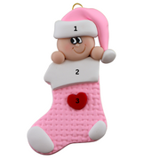 Ornament with infant head in a pink hat poking out of a pink stocking, numbered 1-2 for personalization.