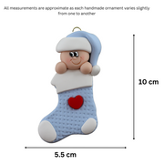 Ornament with infant head in a blue hat poking out of a blue stocking, graphed to show size (5.5x10cm).