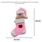 Ornament with infant head in a pink hat poking out of a pink stocking, graphed to show size (5.5x10cm).
