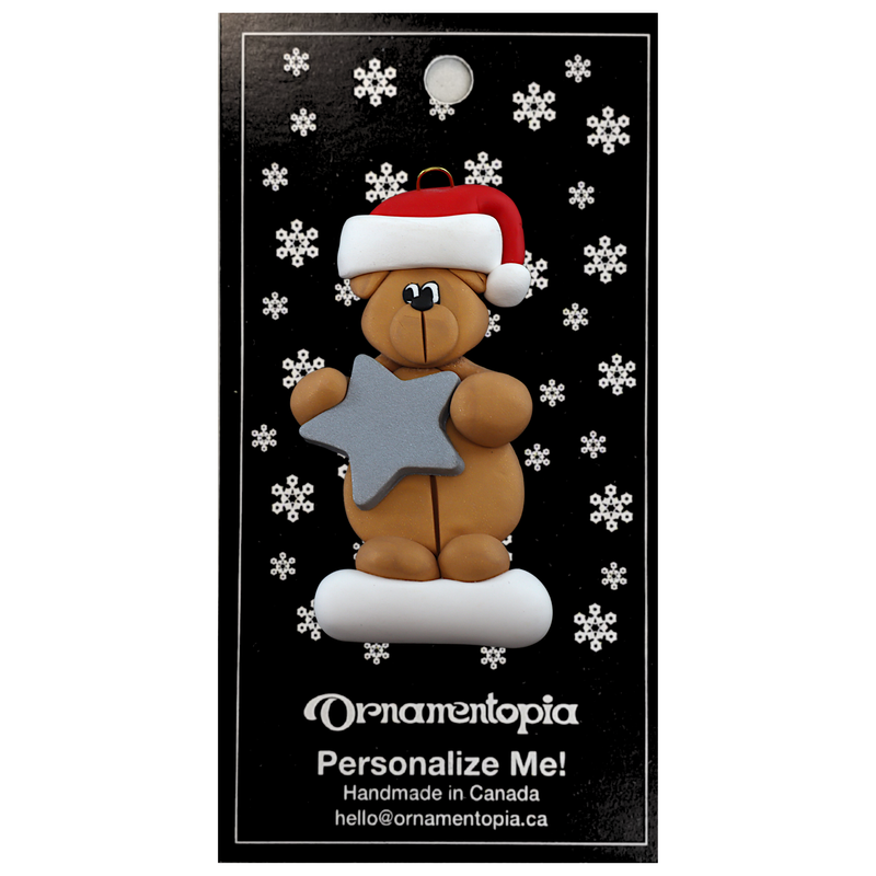 Tan bear in red festive hat holding silver star ornament, on display backing card.