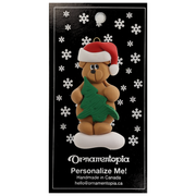 Tan bear in red festive hat holding green tree ornament, on display backing card.