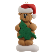 Tan bear in red festive hat holding green tree ornament.