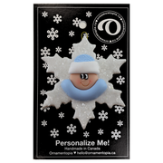 Baby ornament with infant face and blue hat on glittery white snowflake base, on display backing card.