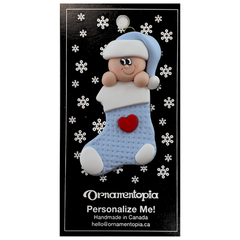 Ornament with infant head in a blue hat poking out of a blue stocking, on display backing card.