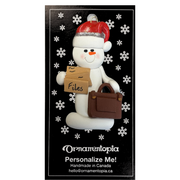 Ornament of white snowman in red hat holding briefcase and files, on display backing card.