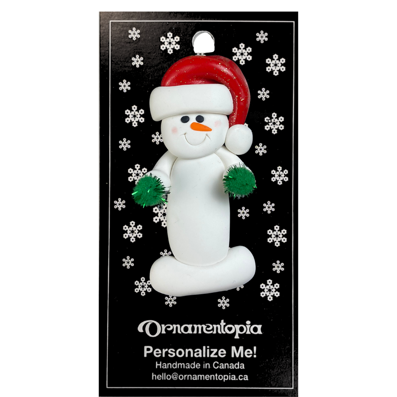 Ornament of white snowman in red hat holding green cheerleader pom-poms, on display backing card.