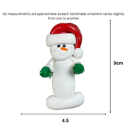 Ornament of white snowman in red hat holding green cheerleader pom-poms, graphed to show size (4.5x9cm).