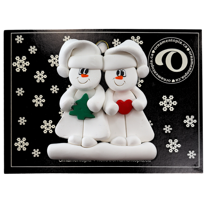 Family ornament with 2 white snowmen in hats, holding holiday objects, on display backing card.