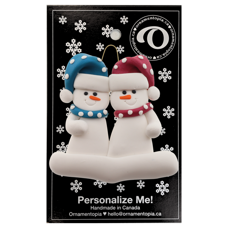 A couple’s ornament of two white snowmen in polka dot scarves and hats, on display backing card.