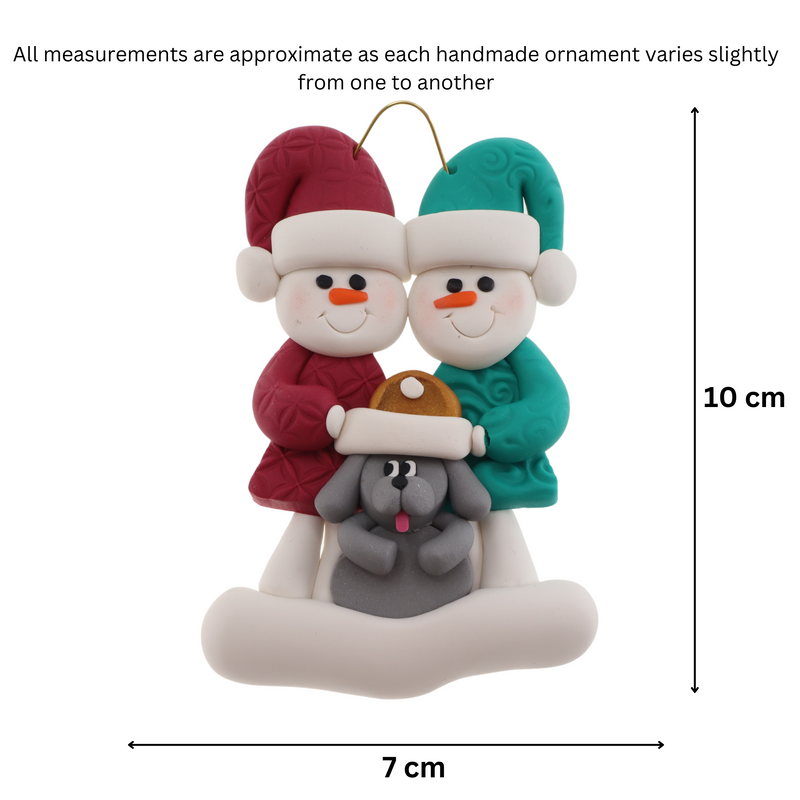 Ornament of snowman couple in red and green shirts and hats with grey dog in Christmas hat, graphed to show size (7x10cm).