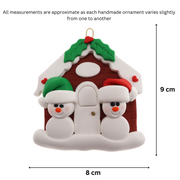 A couple’s ornament of two small white snowmen beside a festive brown house, graphed to show size (8x9cm).