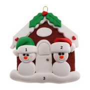 A couple’s ornament of two small white snowmen beside a festive brown house, numbered 1-3 for personalization.