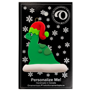 Green dinosaur wearing red festive hat ornament, on display backing card.