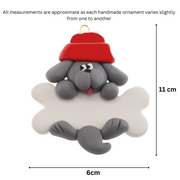 Ornament of grey dog in red hat hanging on a white bone, graphed to show size (6x11cm).