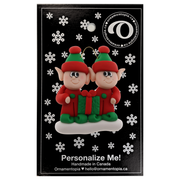 A couple’s ornament with two small red and green elves with a matching present, on display backing card.