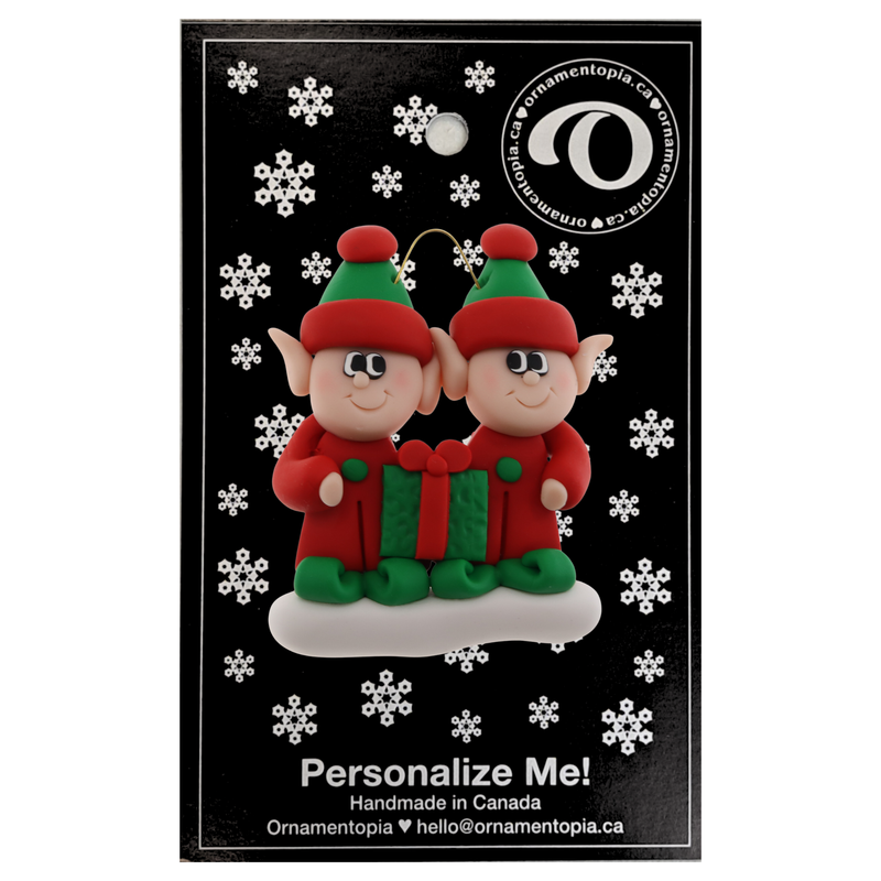 A couple’s ornament with two small red and green elves with a matching present, on display backing card.