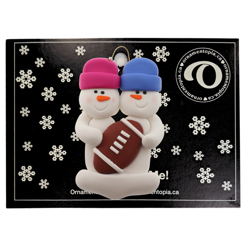 Family ornament with 2 white snowmen in bright hats with a football, on display backing card.