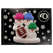 Family ornament with 3 white snowmen in bright hats with a football, on display backing card.