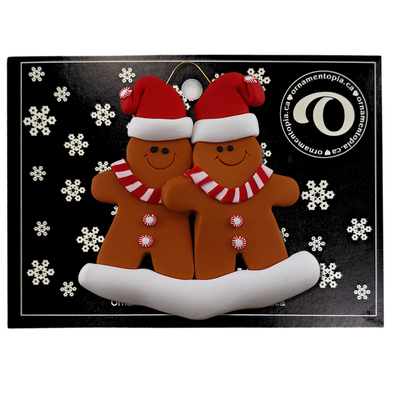 Family ornament with 2 brown gingerbread figures in red Christmas hats, on display backing card.