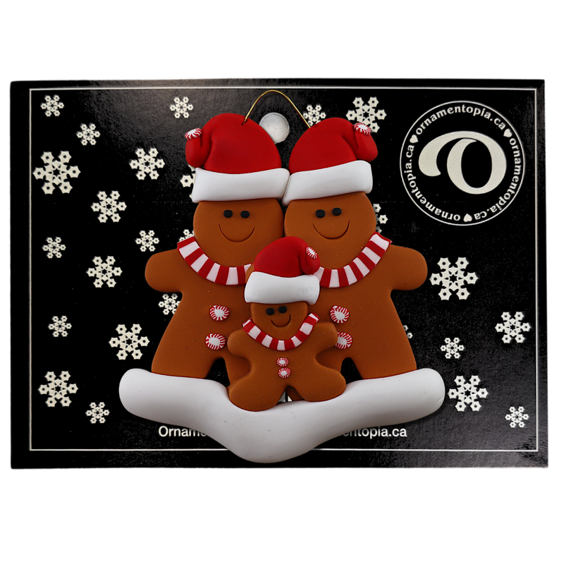 Family ornament with 3 brown gingerbread figures in red Christmas hats, on display backing card.
