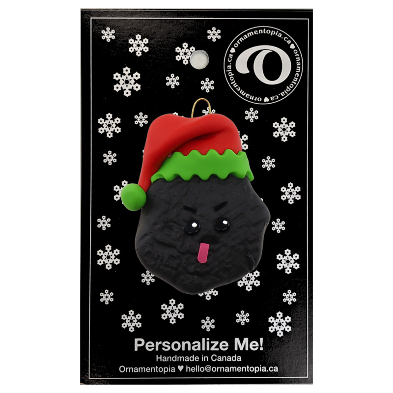 Black frowning lump of coal wearing red festive hat ornament, on display backing card.