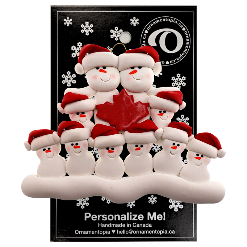 Family ornament with 10 white snowmen in red hats, gathered around a red maple leaf, on display backing card.