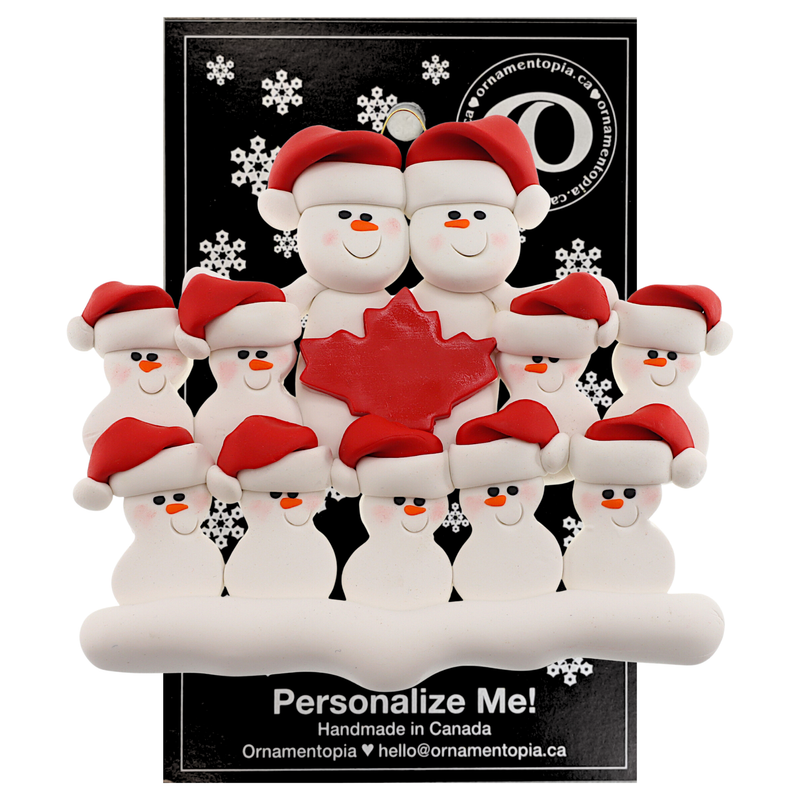 Family ornament with 11 white snowmen in red hats, gathered around a red maple leaf, on display backing card.