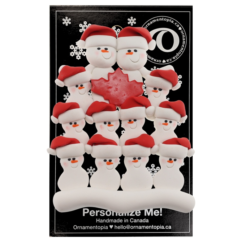 Family ornament with 12 white snowmen in red hats, gathered around a red maple leaf, on display backing card.