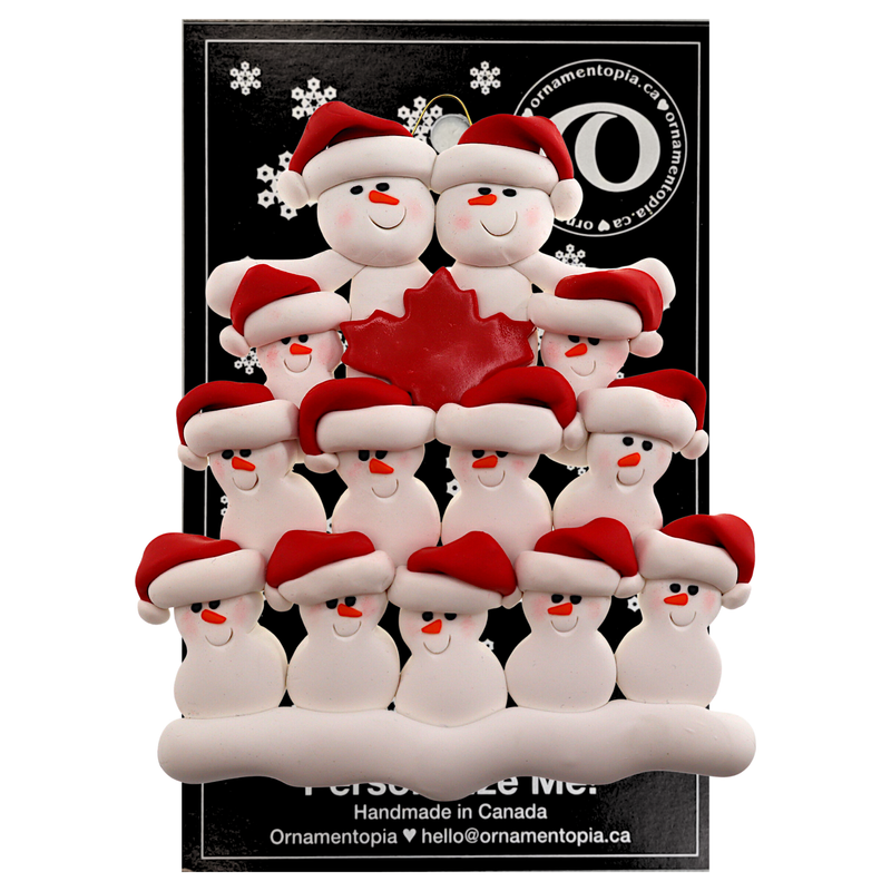 Family ornament with 13 white snowmen in red hats, gathered around a red maple leaf, on display backing card.