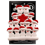 Family ornament with 14 white snowmen in red hats, gathered around a red maple leaf, on display backing card.