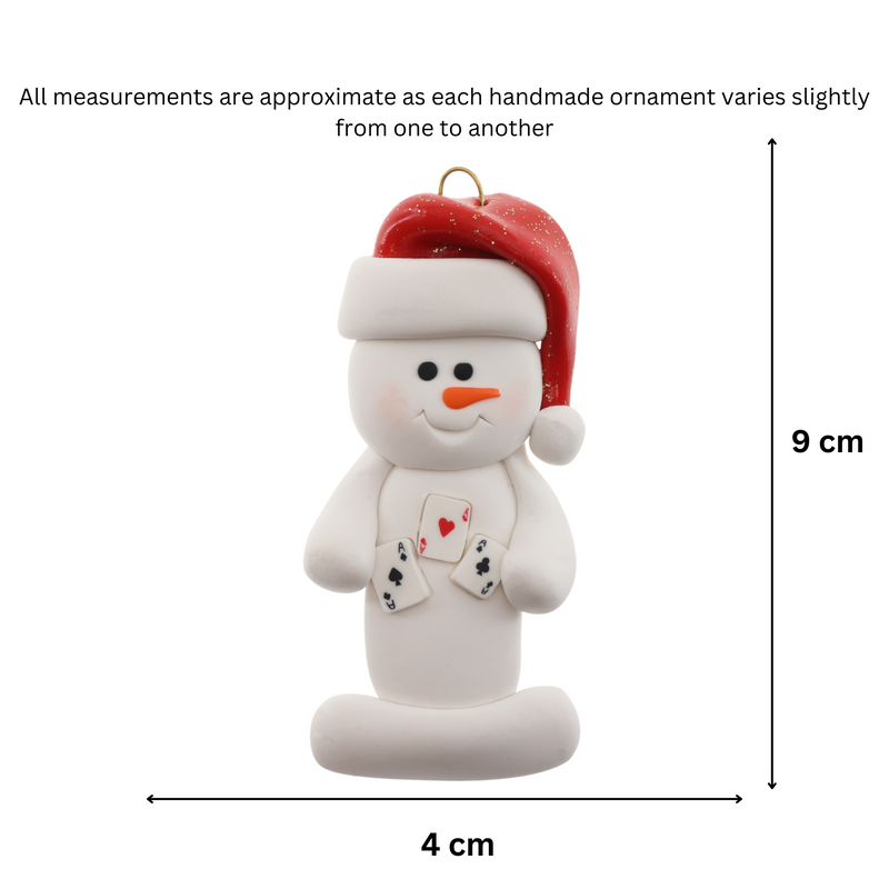 Ornament of white snowman in red hat holding several playing cards, graphed to show size (4x9cm).