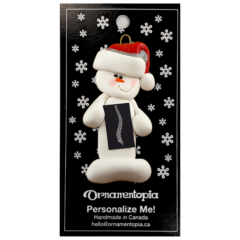 Ornament of white snowman in red hat holding black and white x-ray of a spine, on display backing card.