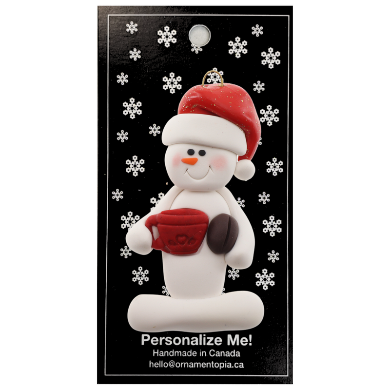 Ornament of white snowman in red hat holding colourful mug and coffee bean, on display backing card.
