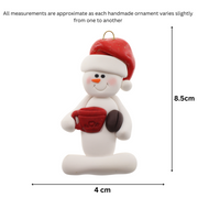Ornament of white snowman in red hat holding colourful mug and coffee bean, graphed to show size (4x8.5cm).