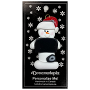 Ornament of white snowman in red hat holding black laptop and a computer mouse, on display backing card.