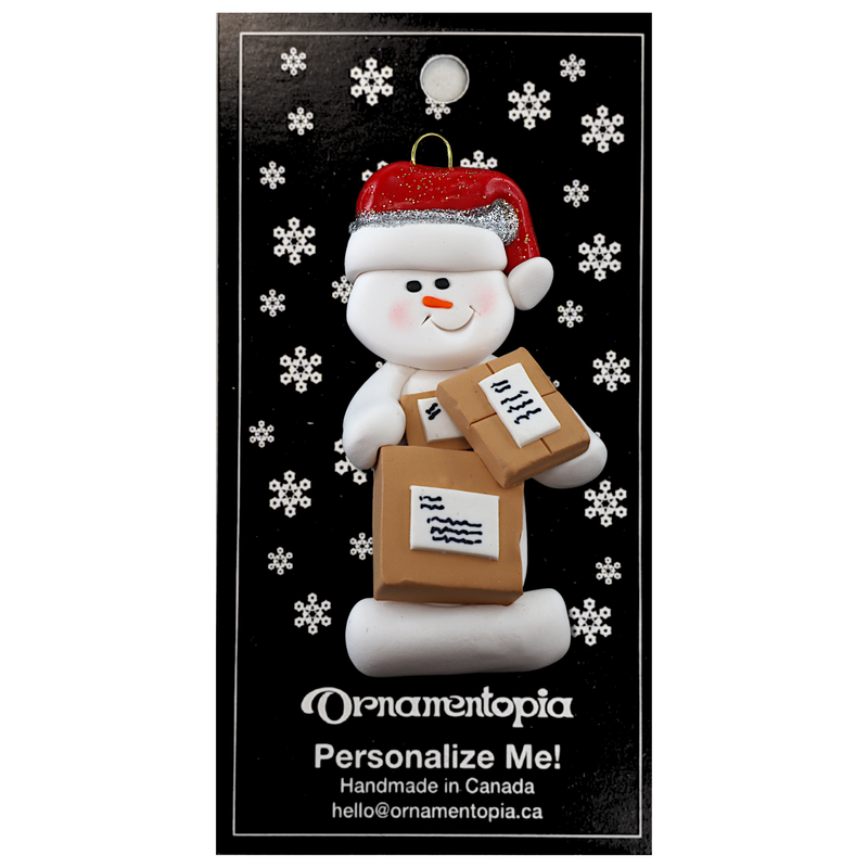 Ornament of white snowman in red hat holding several parcels, on display backing card.