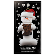 Ornament of white snowman in red hat holding cowboy boots, on display backing card.