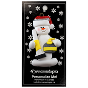 Ornament of white snowman in red hat holding yellow curling stone and broom, on display backing card.
