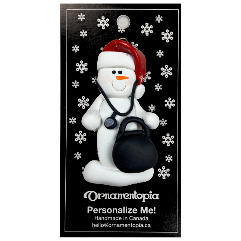 Ornament of white snowman in red hat holding a stethoscope and black medical bag, on display backing card.