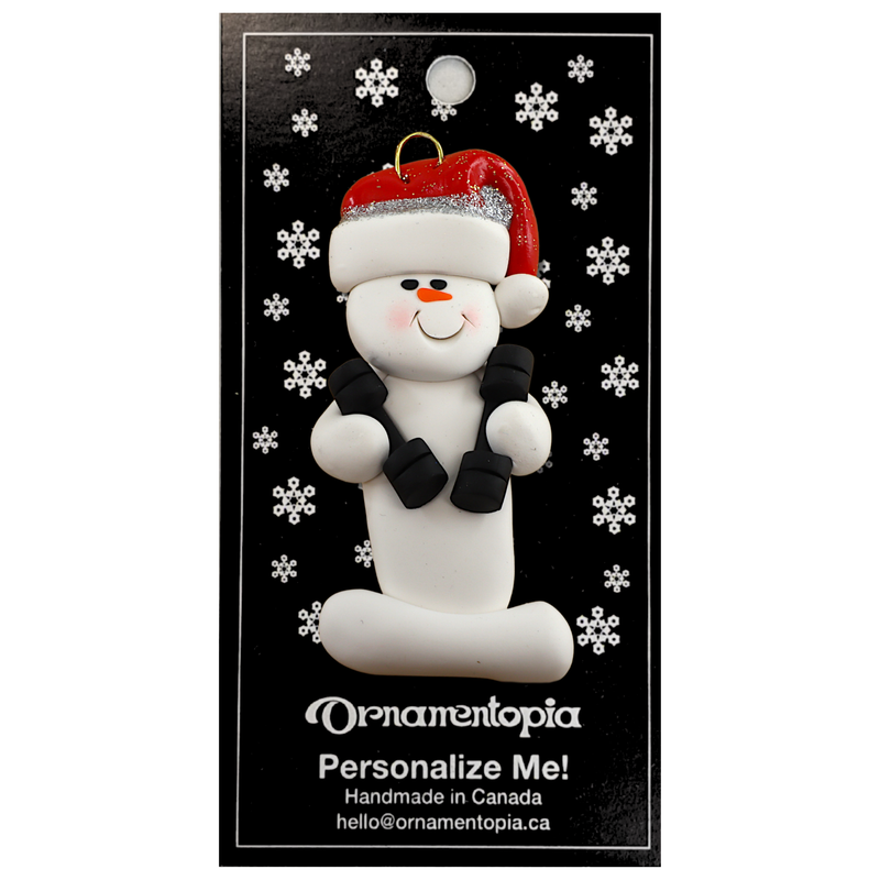 Ornament of white snowman in red hat carrying two dumbbells, on display backing card.
