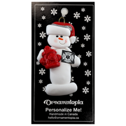 Ornament of white snowman in red hat holding a fire hydrant and firefighter badge, on display backing card.