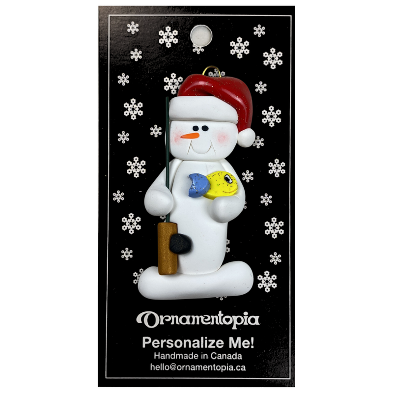 Ornament of white snowman in red hat holding a fishing pole and colourful fish, on display backing card.