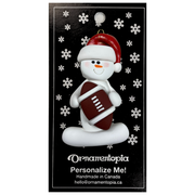 Ornament of white snowman in red hat holding a football, on display backing card.
