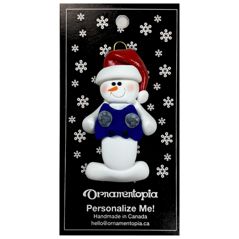 Ornament of white snowman in red hat holding a blue video game controller, on display backing card.