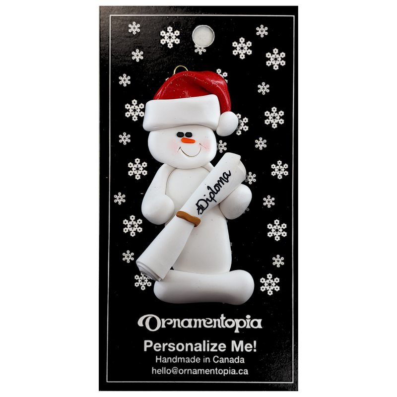 Ornament of white snowman in red hat holding a white diploma, on display backing card.