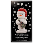 Ornament of white snowman in red hat holding a colourful guitar, on display backing card.