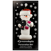 Ornament of white snowman in red hat holding a hairdryer and bottle of hair product, on display backing card.
