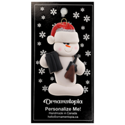 Ornament of white snowman in red hat holding a hunting rifle and pair of binoculars, on display backing card.