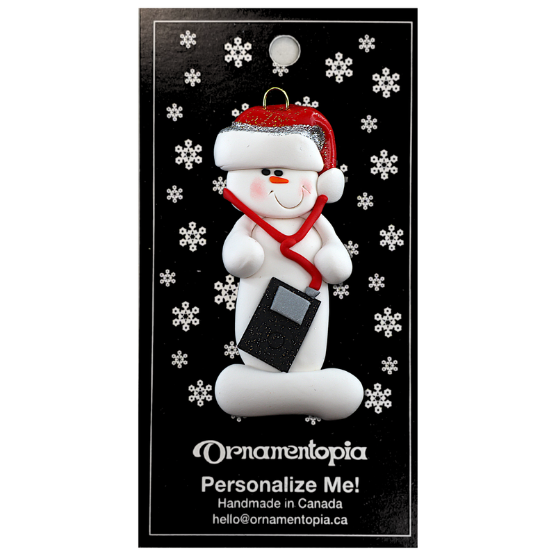 Ornament of white snowman in red hat holding an i-pod with headphones, on display backing card.
